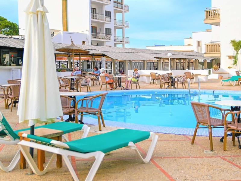 Hotel pool with lounge chairs and tables under a blue sky.