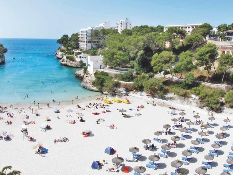 Beach with umbrellas and people in a cove with clear blue water and green vegetation