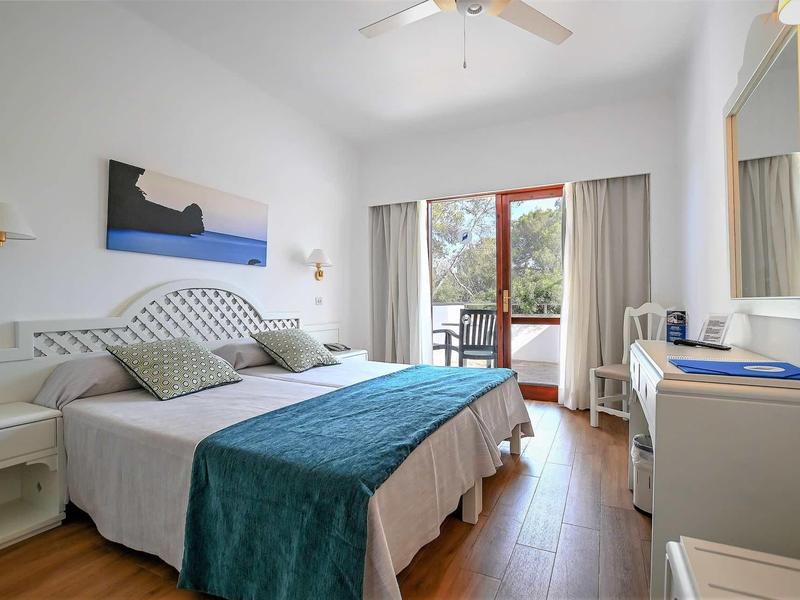 Bright hotel room with double bed, balcony, and wooden flooring.
