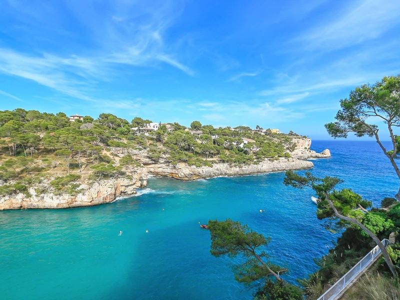 View of a rocky coastline with clear blue water and green vegetation under a blue sky.