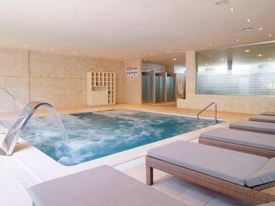 Innen-Pool mit sprudelndem Wasser, Umkleideschränken und grauen Liegen in hellem Raum.