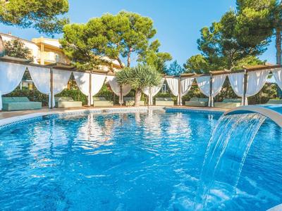 Runder blauer Pool mit Wasserfall und weißen Pavillons im Grünen unter blauem Himmel.