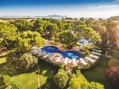 Rundlicher Pool mit Liegen, umgeben von Bäumen und viel grüner Vegetation unter blauem Himmel.