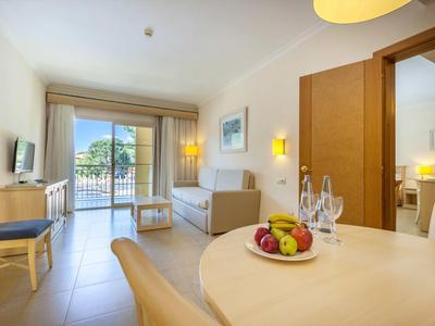 Helles Wohnzimmer mit Balkon, Sofas, Fernseher, Esstisch mit Obst und hellem Parkettboden.