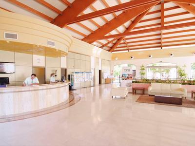 Großzügige, helle Hotellobby mit cremefarbenem Marmorboden, Empfangstresen und roten Holzbalken an der Decke.