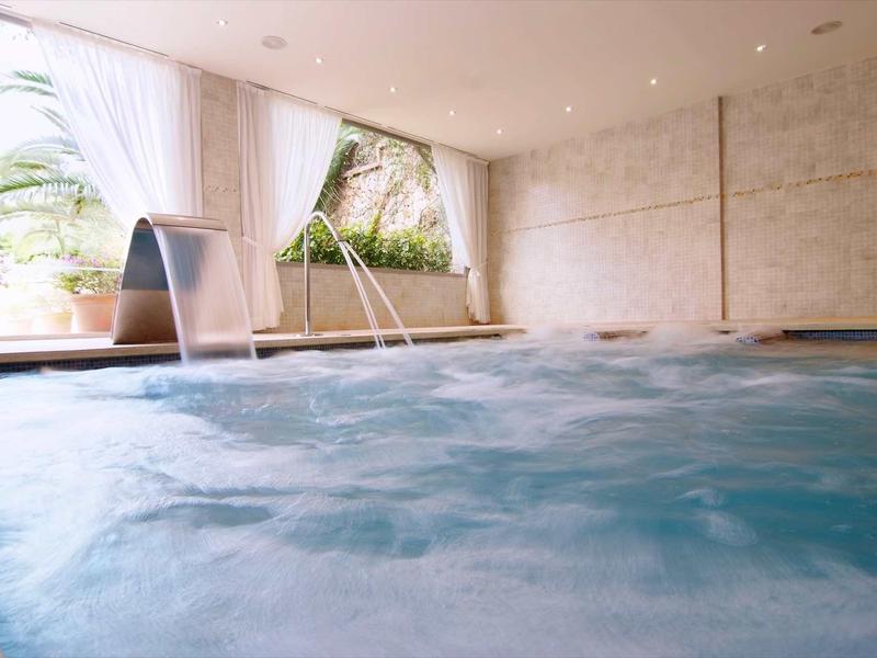 Innenpool mit Wasserspielen, großen Fenstern und warmem, hellem Licht.