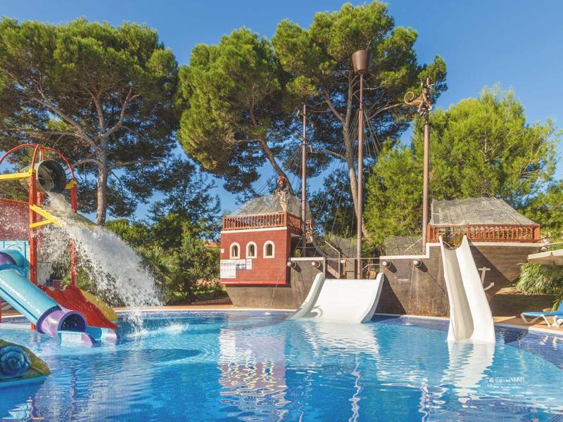 Freizeitbad mit Wasserrutschen, einem Spritzspiel und Bäumen im Hintergrund bei klarem Himmel.