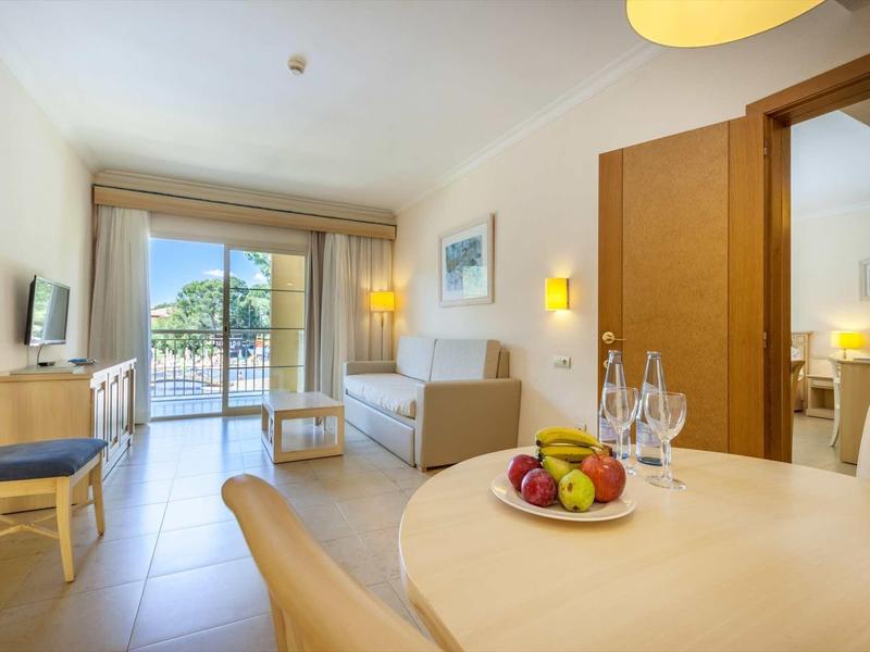 Helles Wohnzimmer mit Balkon, Sofas, Fernseher, Esstisch mit Obst und hellem Parkettboden.