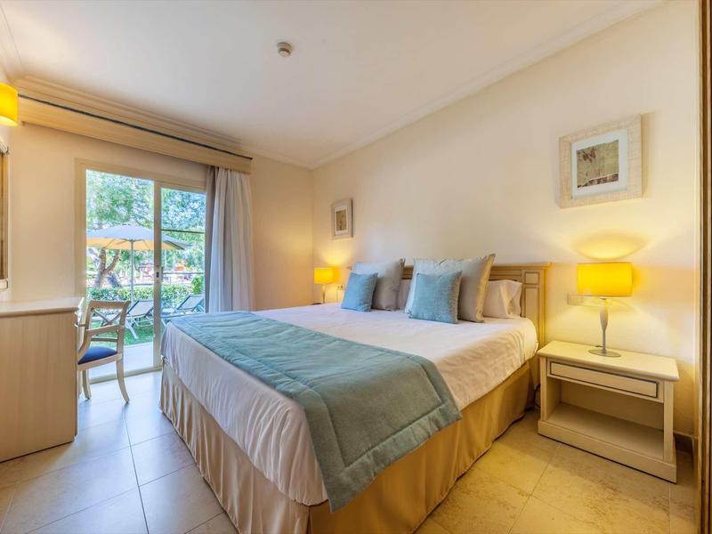 Helles Schlafzimmer mit Doppelbett, zwei Nachttischen, Lampen und Balkon mit Blick ins Grüne.