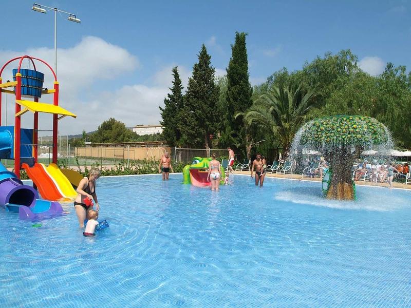 Wasserpark mit bunten Rutschen, Planschbecken, Wasserspiel und grüner Umgebung bei Sonnenschein.
