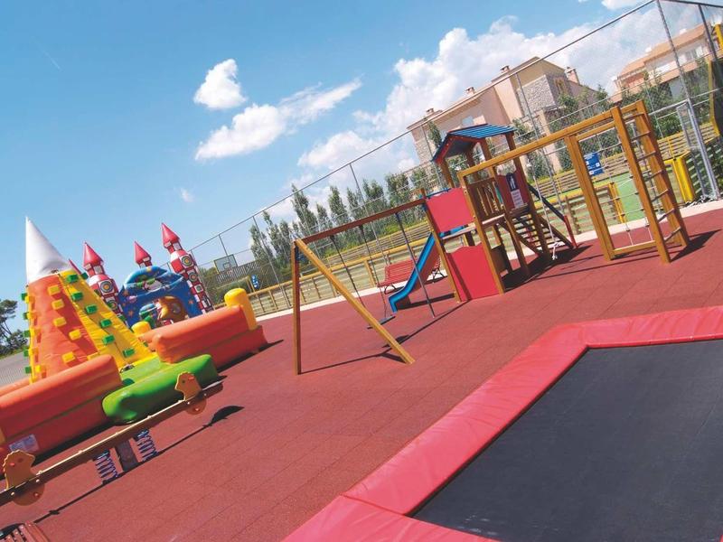 Bunter Kinderspielplatz mit Klettergerüst, Trampolinen und Hüpfburg unter blauem Himmel.