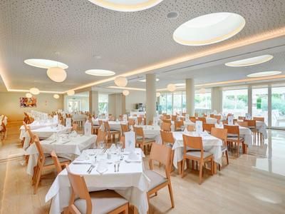 Heller Speisesaal mit runden Deckenleuchten, Holzstühlen und weiß gedeckten Tischen.