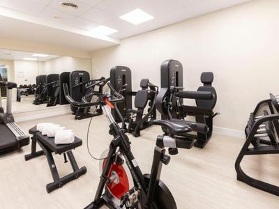 Kleiner Fitnessraum mit Spinningbike, verschiedenen Kraftgeräten und Handtüchern auf Bank.