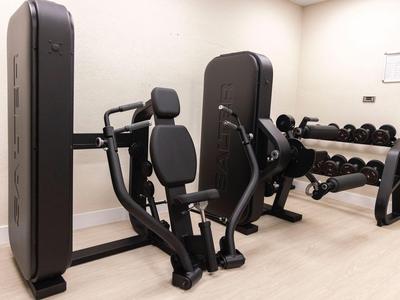 Moderner Fitnessraum mit Krafttrainingsgeräten und Hanteln in hellem Raum.