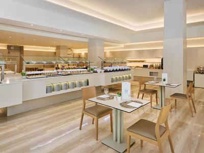 Ristorante d'hotel moderno e luminoso con sedie in legno e area buffet sotto illuminazione a soffitto.