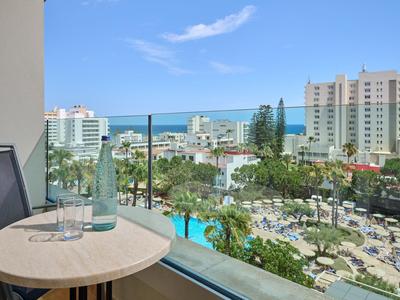 Balcone con bottiglia di vetro e bicchiere, vista su piscine e mare in un resort.
