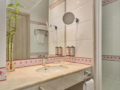Bagno luminoso in hotel con lavabo, specchio, pianta di bambù e cabina doccia.