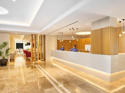 Reception di un hotel moderno con illuminazione luminosa, pavimento in marmo liscio e personale cordiale.