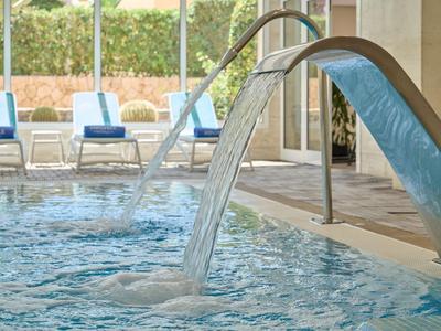 Piscina moderna dell'hotel con fontane d'acqua e sedie a sdraio blu sullo sfondo.
