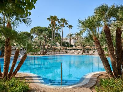 Piscina azzurra limpida circondata da palme e vegetazione in un resort per vacanze.