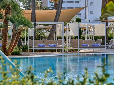Piscina con ombrelloni e lettini davanti a un edificio alberghiero.