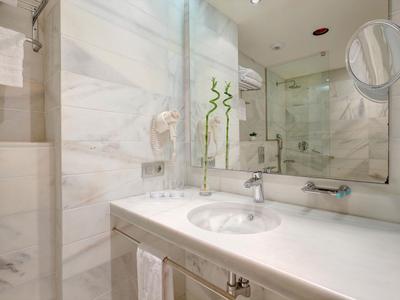 Bagno moderno con pareti in marmo bianco, lavabo, specchio e doccia in vetro.