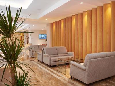 Lobby dell'hotel con divani grigi, pannelli in legno e piante verdi in design moderno.