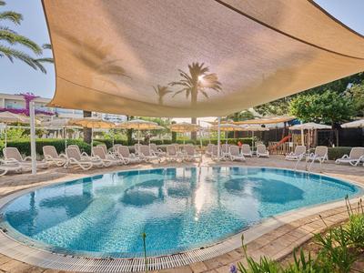 Piscina rotonda dell'hotel con superficie d'acqua blu e vele parasole, circondata da sedie a sdraio.
