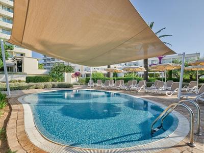 Piscina rotonda con tenda parasole e lettini in un contesto alberghiero.