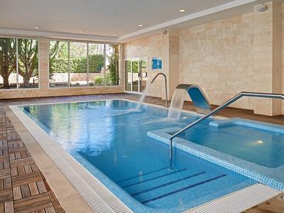 Innen-Schwimmbad mit blauem Wasser, Holzfliesenboden und großen Fenstern zum Garten.