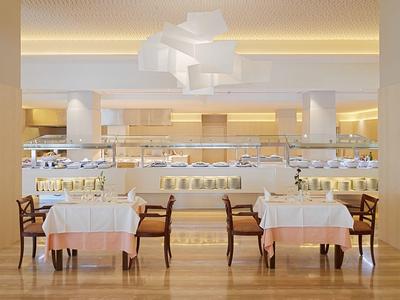 Helles, elegantes Restaurant mit weißen Tischen, Holzboden und moderner Deckenbeleuchtung.