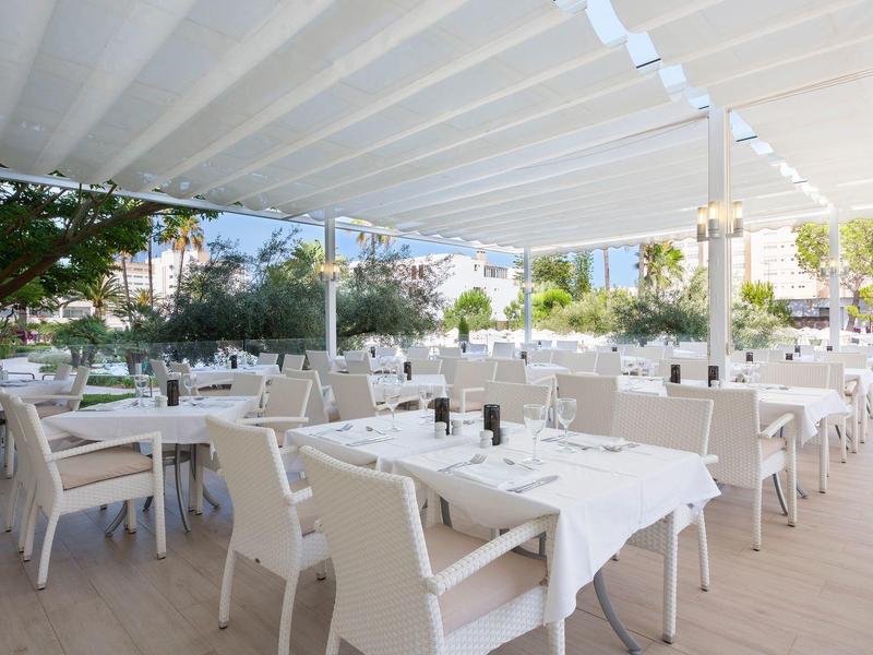 Helle Terrasse mit weiß gedeckten Tischen und Stühlen unter einem Sonnendach.