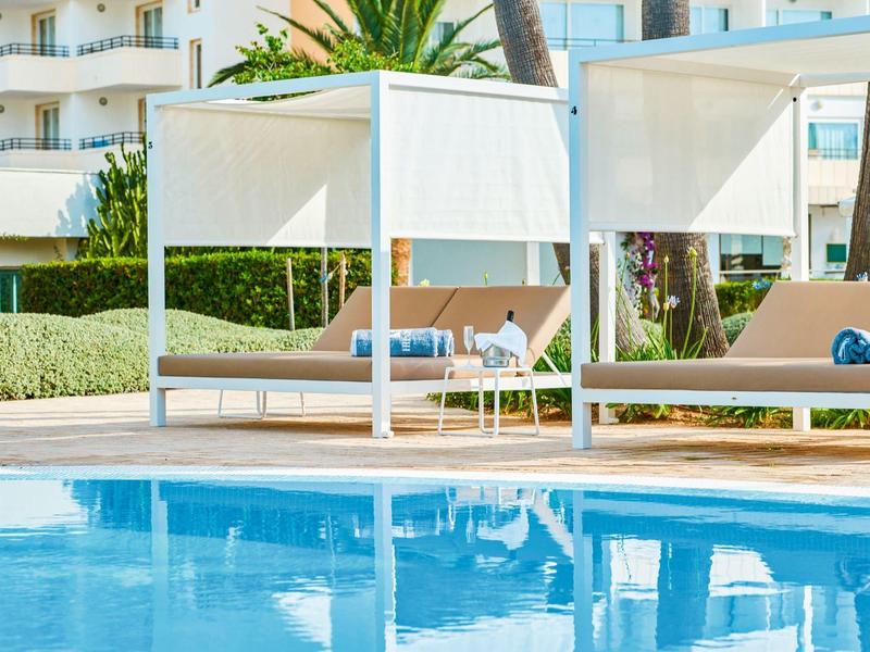 Zwei weiße Poolbetten mit Baldachin neben einem blauen Schwimmbecken im Hotelgarten.