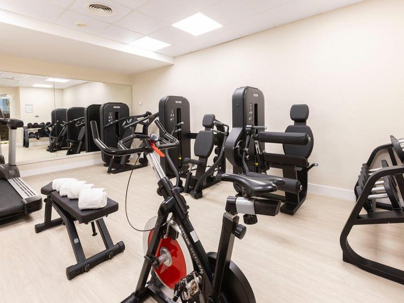 Moderner Fitnessraum mit verschiedenen Trainingsgeräten und Spiegelwand.