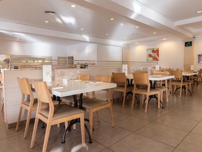 Helles, modernes Restaurant mit Holztischen und Stühlen, weiße Wände und Decke.