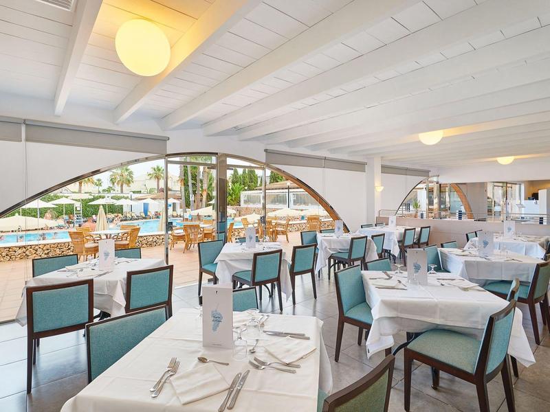 Helles Restaurant mit weißen Tischen, türkisfarbenen Stühlen und Ausblick auf den Poolbereich.