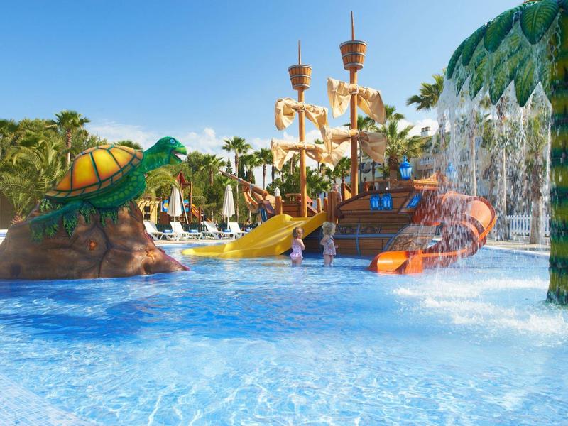 Bunter Kinderspielplatz auf Wasser mit Rutsche und künstlichen Palmen im Schwimmbad.