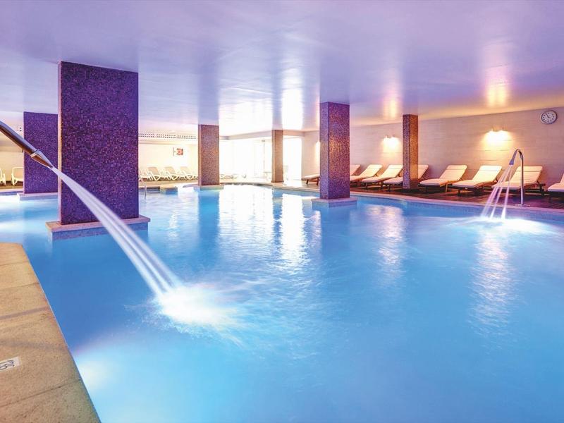 Jasny basen kryty z wodnymi strumieniami i wygodnymi leżakami wokół.