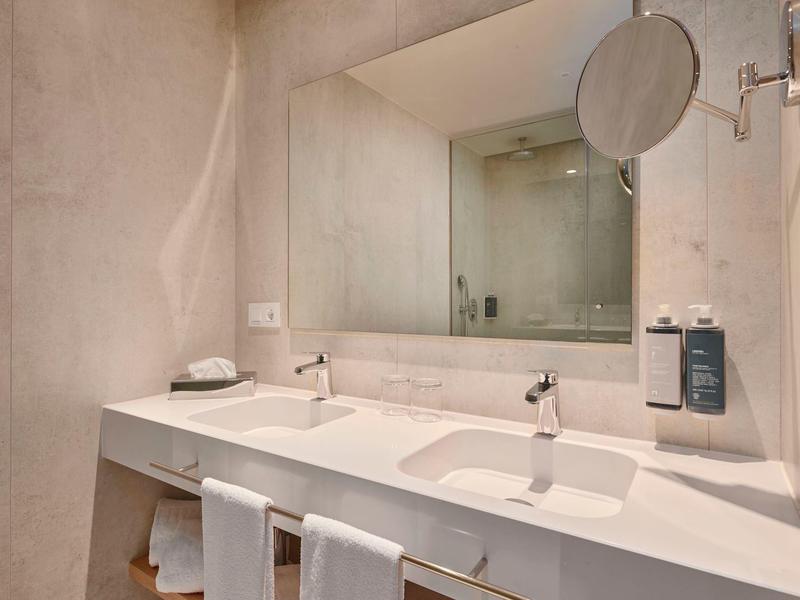 Nowoczesna podwójna umywalka z dużym lustrem i ręcznikami w jasnej łazience.