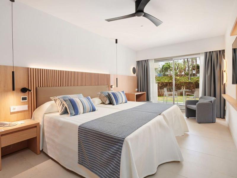 Nowoczesny pokój hotelowy z dużym łóżkiem, fotelami i dużym oknem z widokiem na ogród.