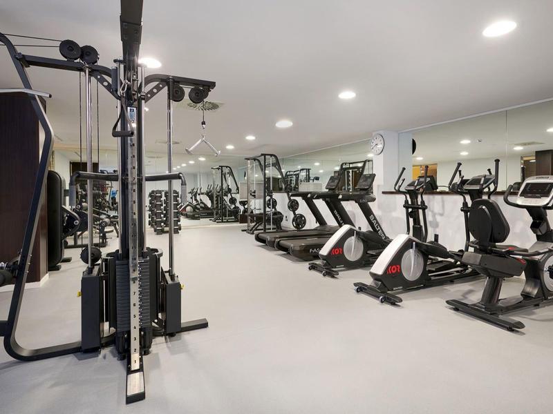 Nowoczesna siłownia z różnymi urządzeniami do ćwiczeń w jasnym, zadbanym pomieszczeniu.