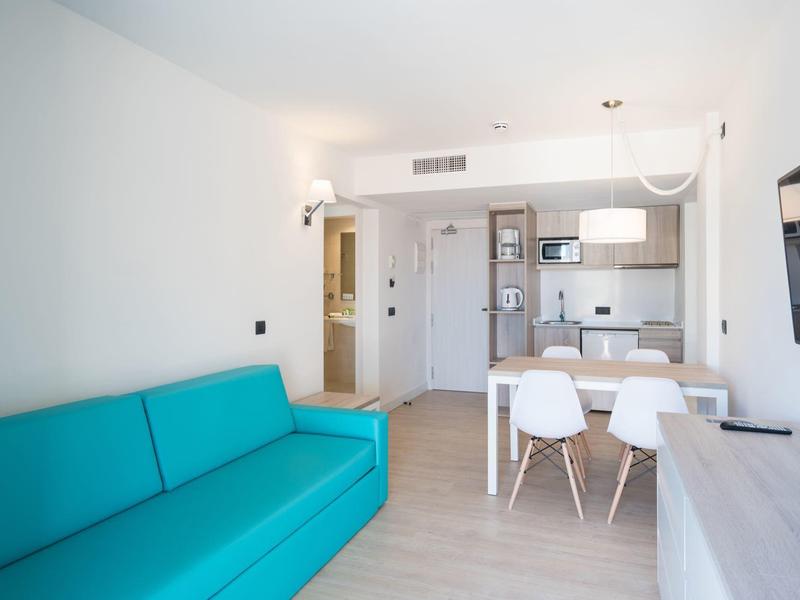 Modern living area with blue sofa, dining table with white chairs, and open kitchen in bright apartment.