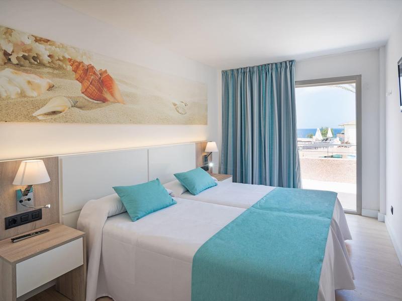 Modern hotel room with double bed, blue bedding, wall art, and terrace access with sea view.