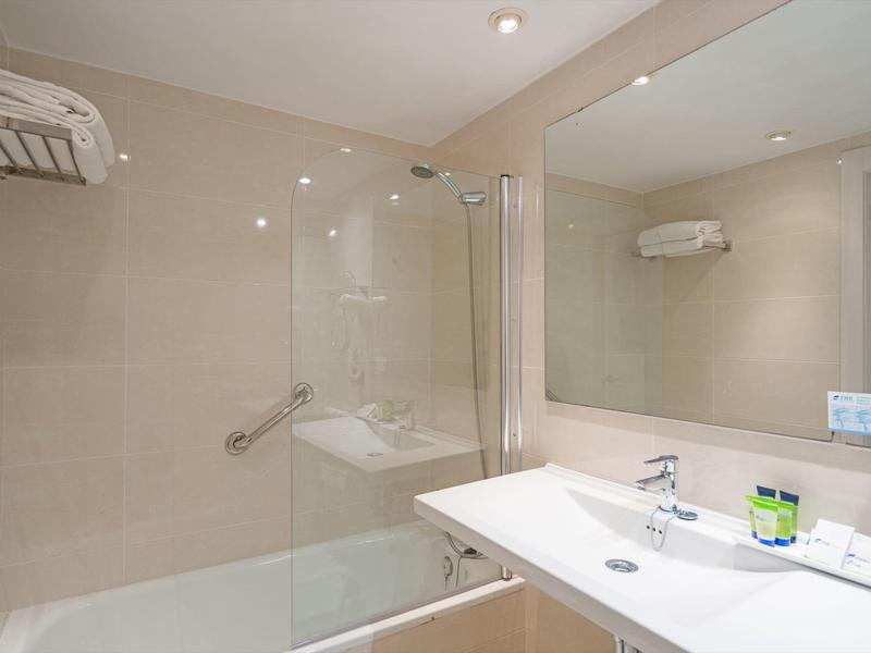 Bright bathroom with large mirror wall, sink, and glass shower partition.
