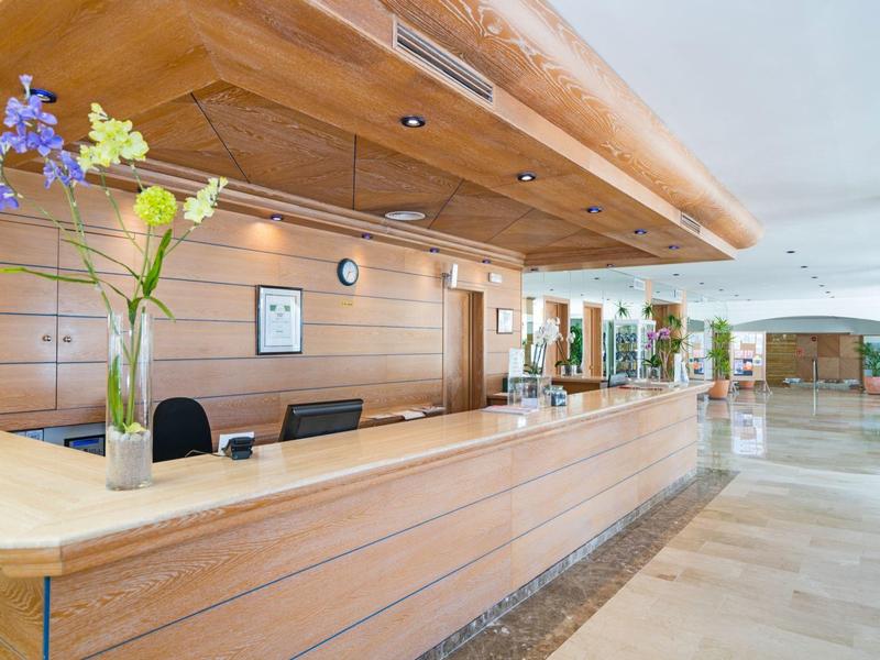 Bright hotel lobby with a long wooden reception desk and flowers in a vase.