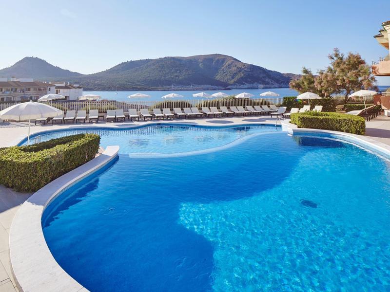 Large outdoor pool with sun loungers and mountain views under clear sky.