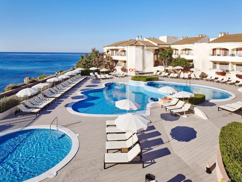 Outdoor pool area with sun loungers and sea view under a clear sky.