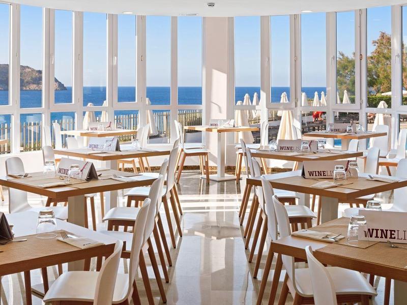 Bright, modern restaurant with many wooden tables and chairs, large windows with sea view.