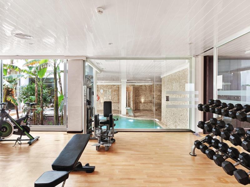 Modern gym with dumbbells, exercise equipment, and glass wall overlooking the pool area