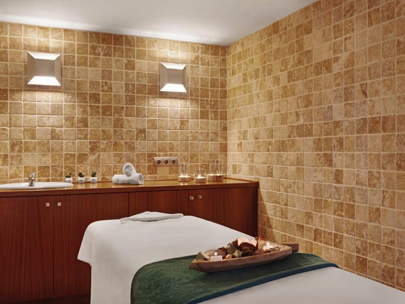 Treatment room with massage table, warm wooden cabinets, and stone-patterned walls.